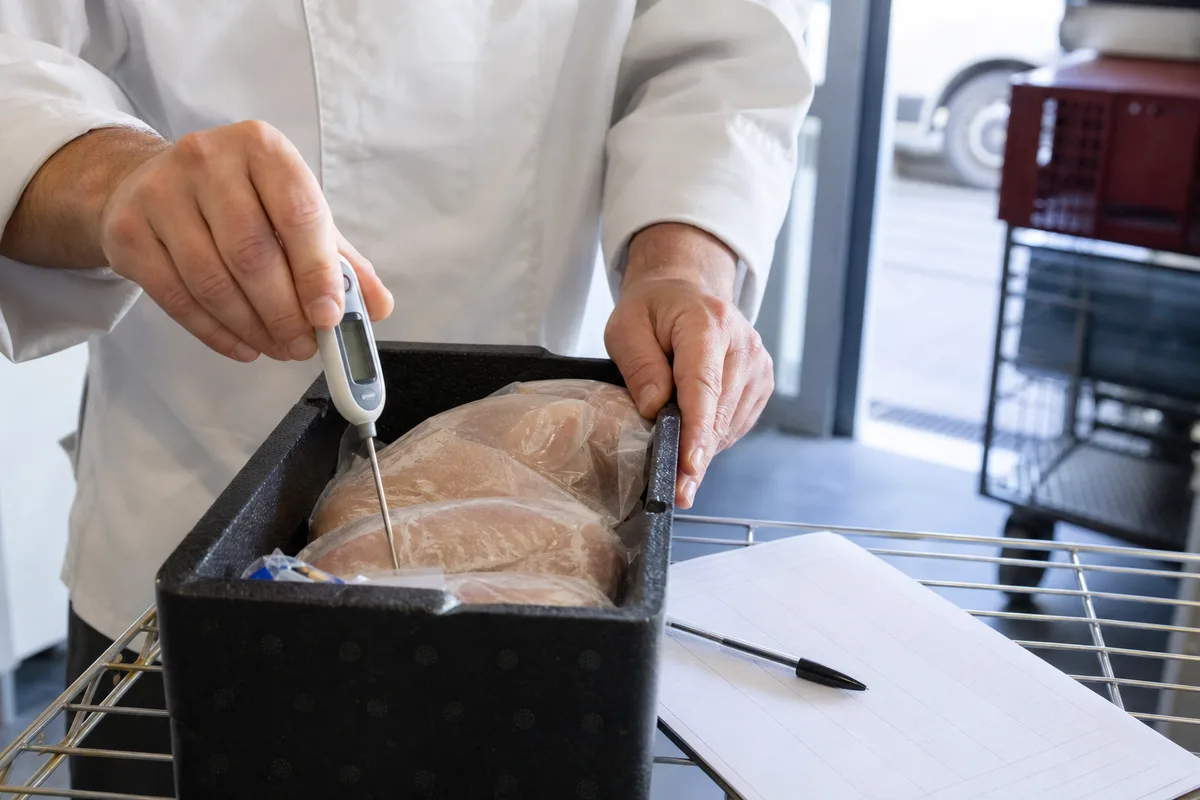 Cuisinier contrôlant la température d’une caisse de produits frais avec un thermomètre sonde
