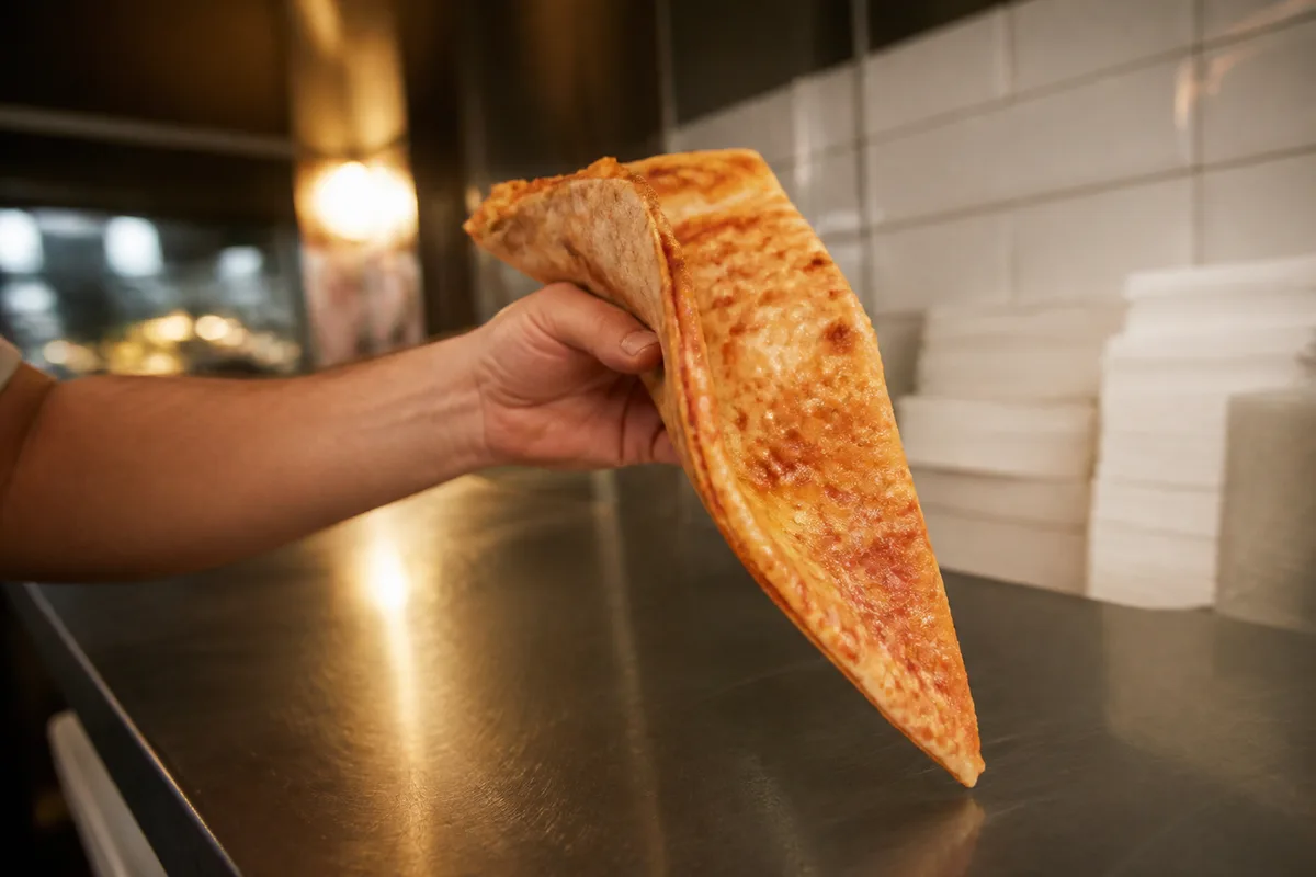 Part de pizza fine pliée en deux tenue au-dessus d’un comptoir de pizzeria new-yorkaise