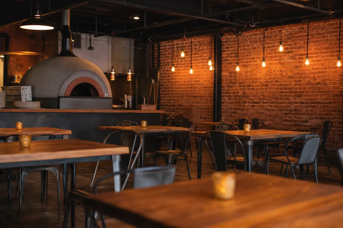 Salle de pizzeria au style industriel, mur de brique apparente et suspensions métalliques